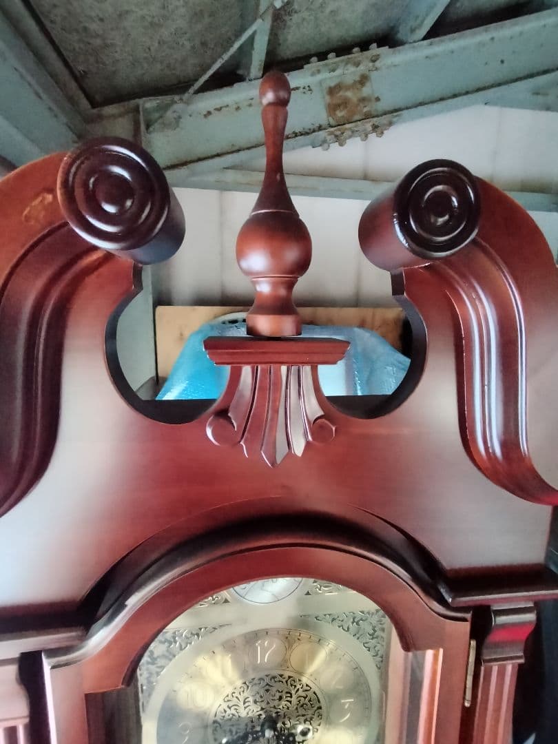 装飾的な文字盤と振り子を持つダークウッドの柱時計